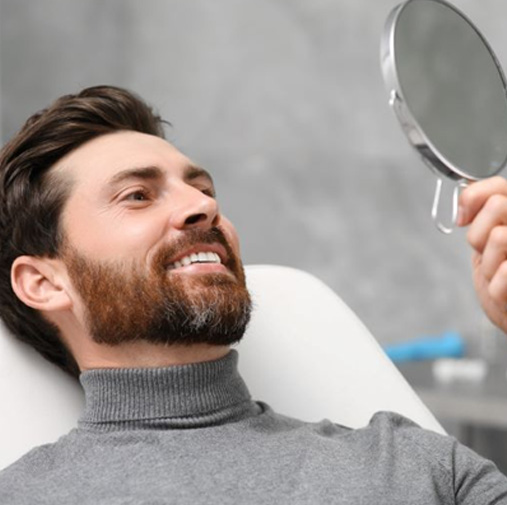 Dental patient holding mirror, looking at his smile